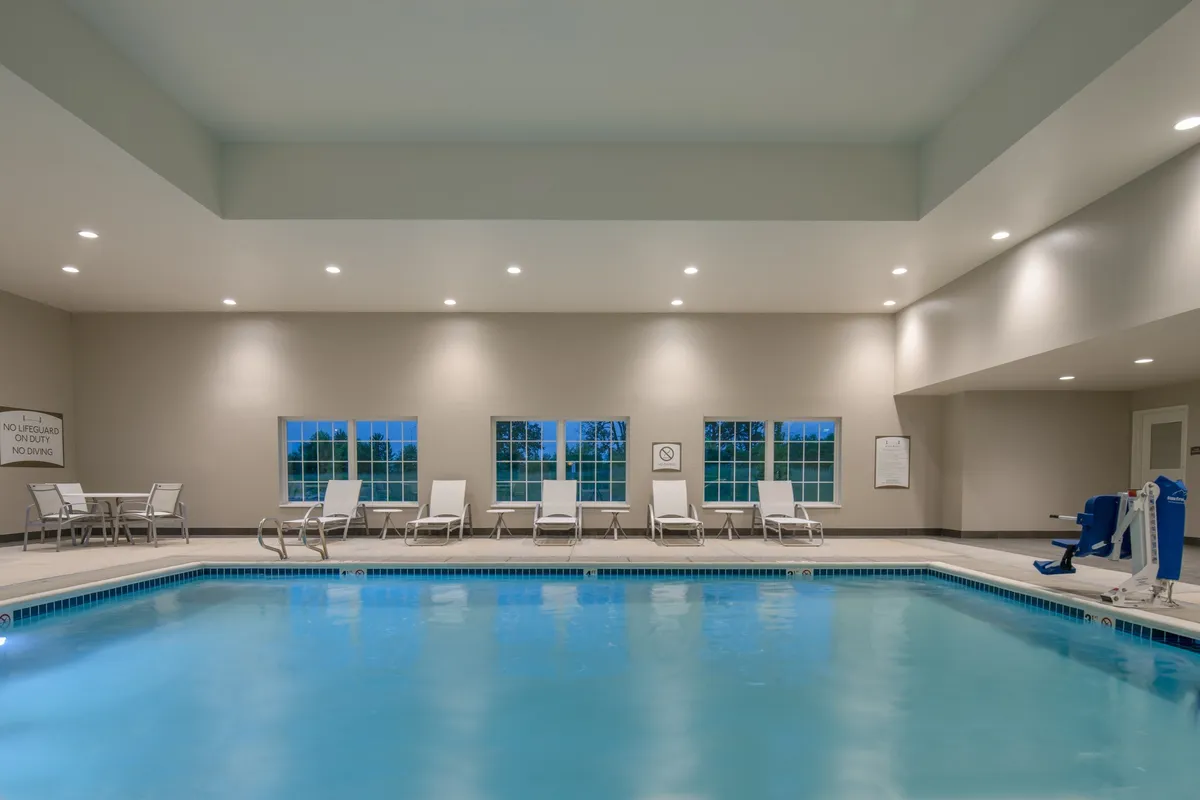 An inviting indoor swimming pool is flanked by comfortable lounge chairs and large windows that let in natural light, creating a tranquil space for relaxation or a refreshing swim. The area is clean and well-maintained, ideal for both families and fitness enthusiasts.