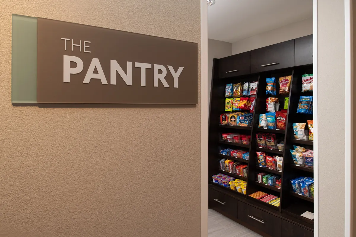 This image features 'THE PANTRY'—a well-stocked snack area with shelves of treats—offering a casual, communal space where guests can pick up refreshments and socialize.