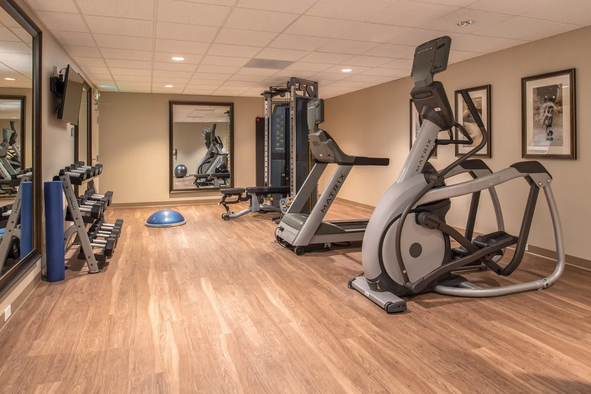 A modern fitness center equipped with a variety of exercise machines, mirrored walls, wooden flooring, and vibrant wall art. The space is bright and energetic, inviting guests to start their day with a workout or pursue their personal wellness journey.